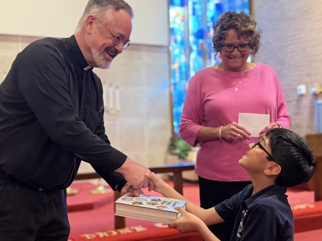 Pastor congratulates boy receiving book at Redeemer Lutheran School