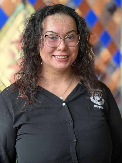 Cora Dunkin, a woman with curly dark hair and glasses, smiles at the camera.