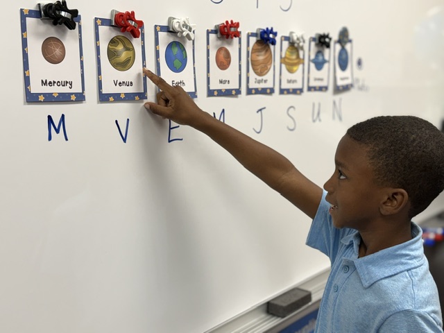 Young boy points to Venus on a classroom solar system chart