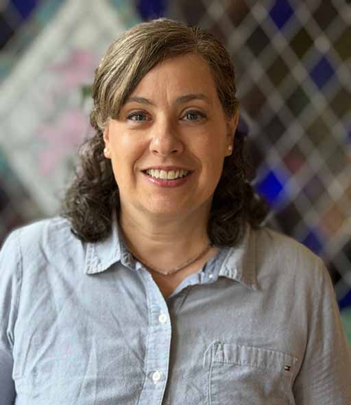 Natalie Pugh, smiling, wearing a blue collared shirt.