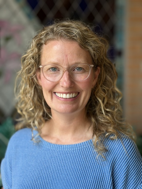 Ashley Riegler, smiling woman with curly blonde hair and glasses