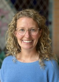 Ashley Riegler, smiling woman with curly blonde hair and glasses