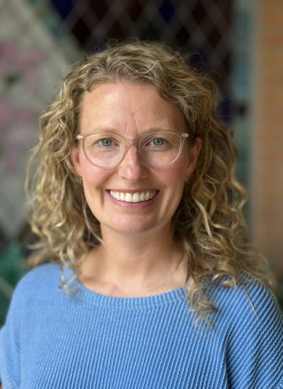 Ashley Riegler, smiling woman with curly blonde hair and glasses