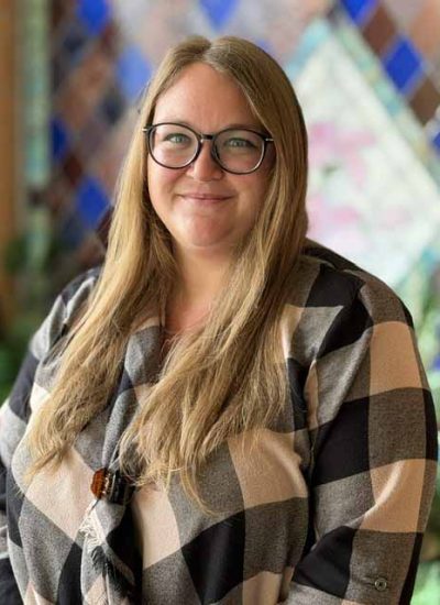 Ashley Robbins, a woman with blonde hair and glasses, smiles at the camera.