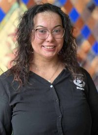 Cora Dunkin, a woman with curly dark hair and glasses, smiles at the camera.