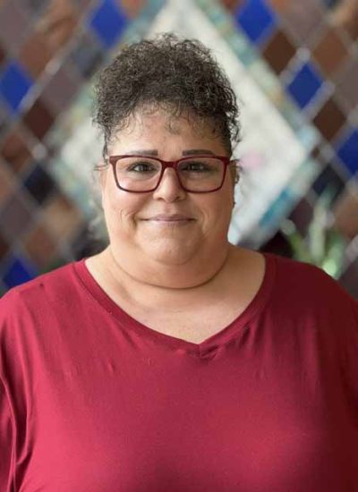 Karen Simmons, a woman with curly hair and glasses, smiles in a red shirt.