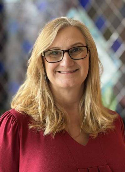 Sharon Johnson, a smiling woman with blonde hair and glasses, wearing a red shirt.